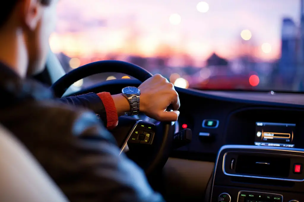 Chauffeur's hands on the steering wheel with city lights ahead